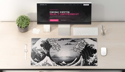 Desk setup with monitor, keyboard, white mouse, potted plant, and large black and white wave-patterned desk mat